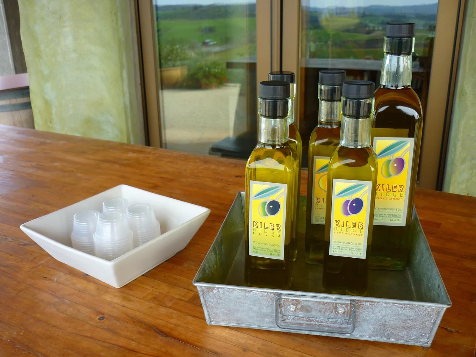 Bottles of Kiler Ridge extra virgin olive oil displayed on a wooden table with a scenic view of the rolling hills of Paso Robles in the background